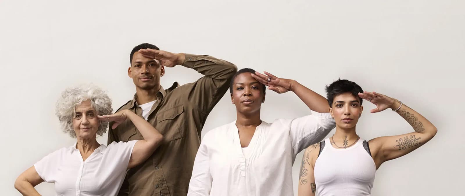 Four people stand against a white background, saluting. They have diverse appearances and are wearing casual, neutral-colored clothing.
